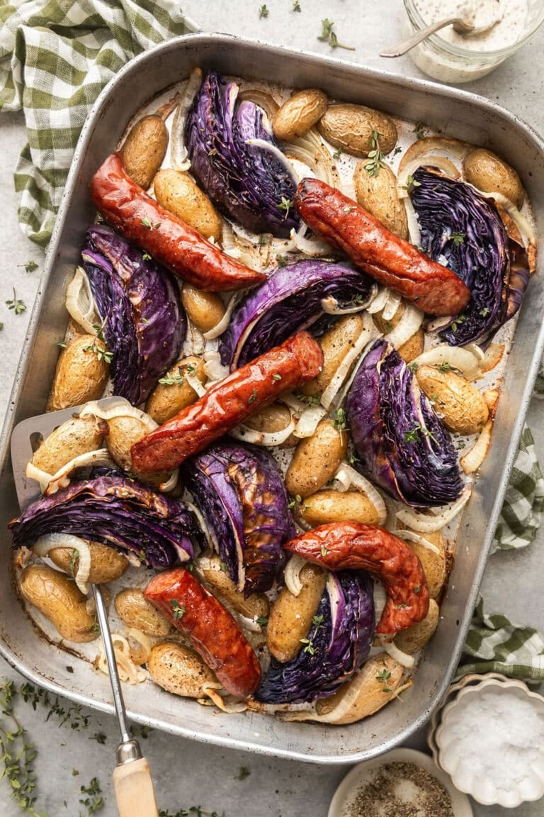Overhead view of a sheet pan of Kielbasa and Potatoes with purple cabbage wedges.