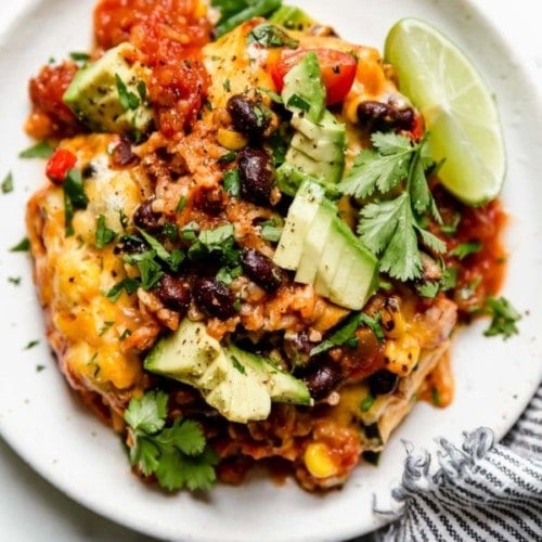A serving of healthy taco casserole on white plate, topped with diced avocado, tomatoes, and fresh cilantro.