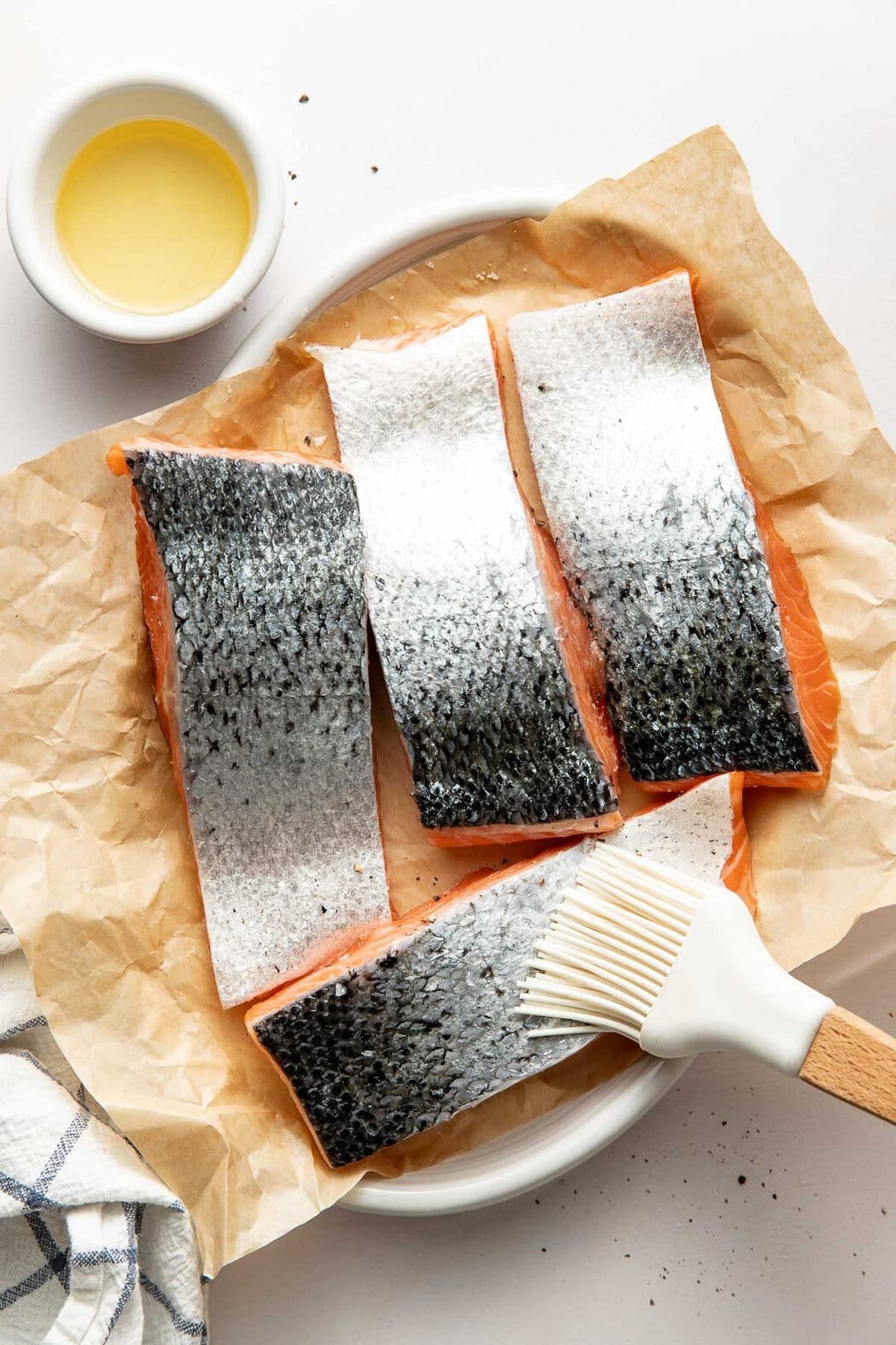 Overhead view of salmon fillets laying skin side up with a brush oiling the skin.
