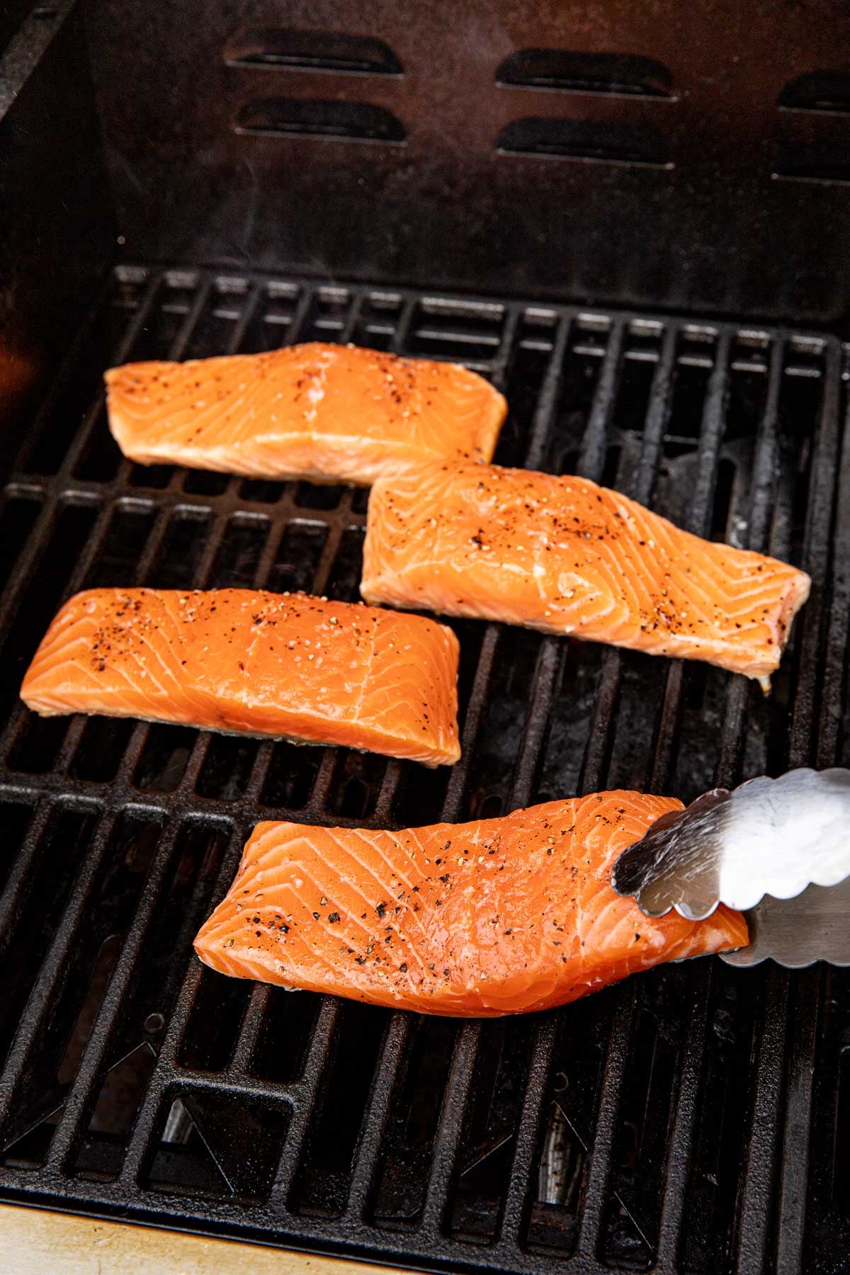 Close up view of salmon fillets on a grill topped with salt and pepper.