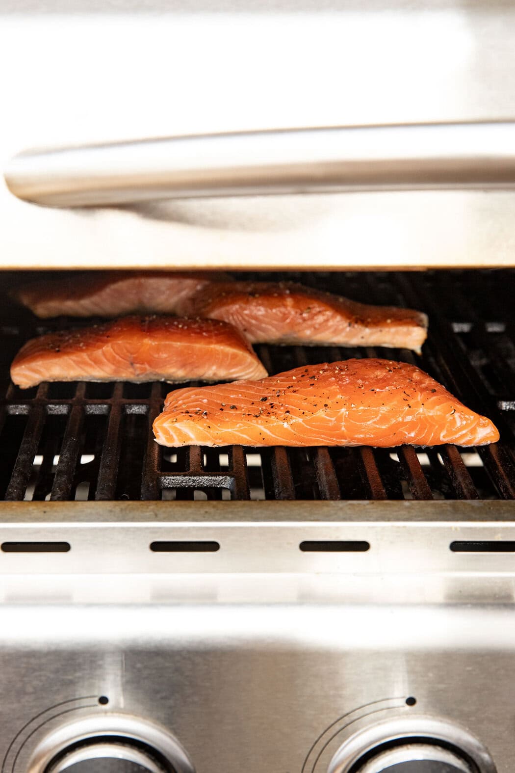 Side view of salmon fillets on a grill topped with salt and pepper.
