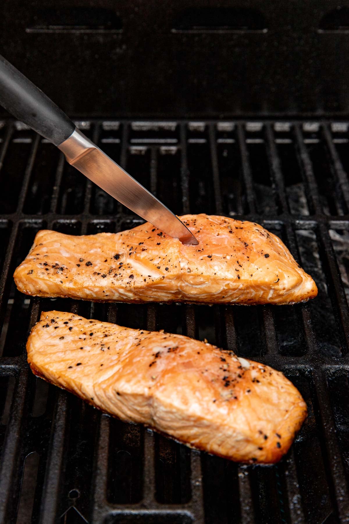 Close up view of salmon fillets on a grill with a knife checking the center for doneness.