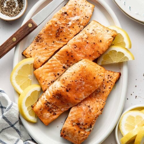 Overhead view of an oval platter filled with Grilled Salmon fillets garnished with lemons