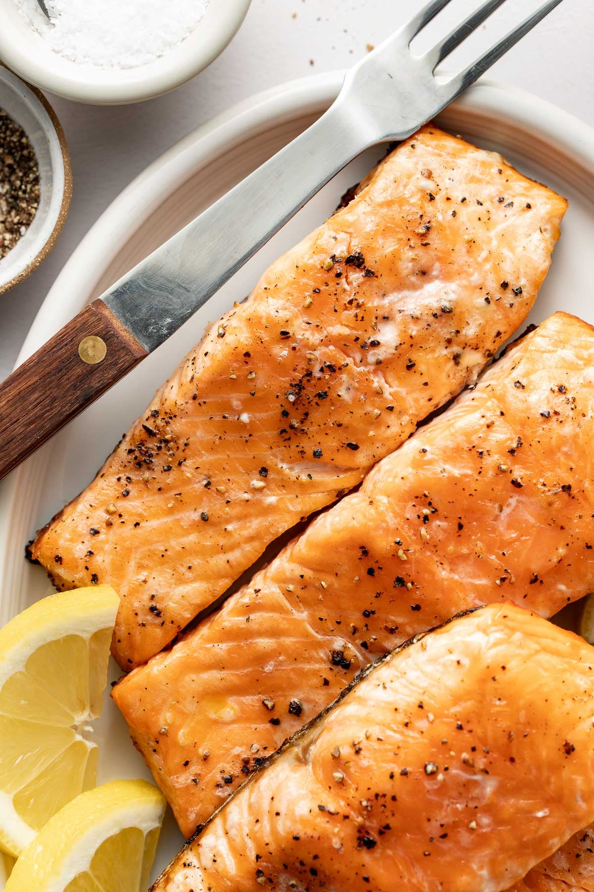 Close up view of Grilled Salmon fillets sprinkled with black pepper and garnished with lemon wedges.