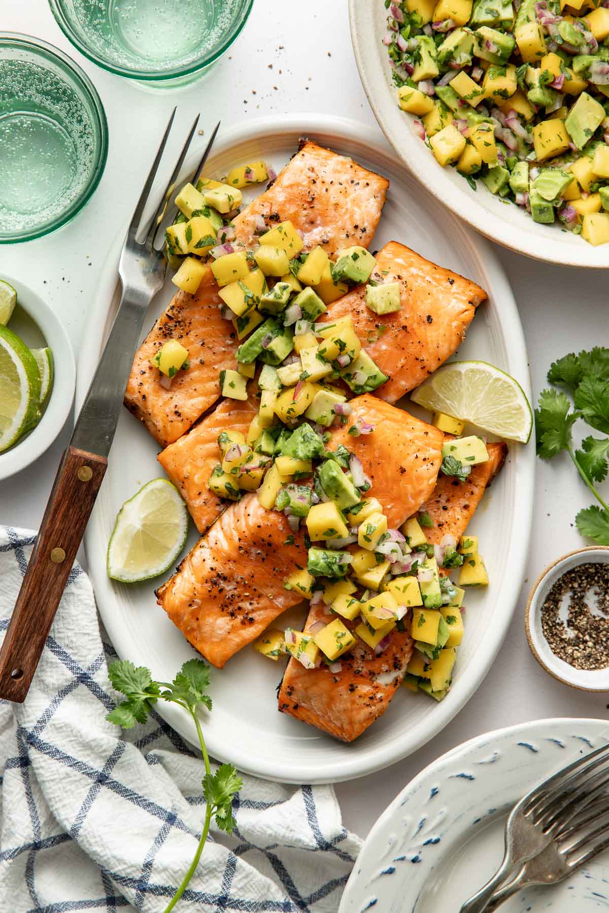 Overhead view of an oval platter filled with Grilled Salmon fillets topped with a fresh mango salsa and garnished with limes.