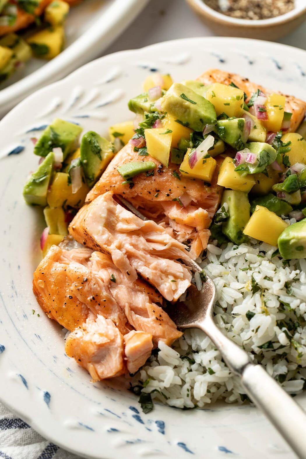 Close up view of a plate of rice, grilled salmon, and a fresh mango salsa topped with fresh cilantro.