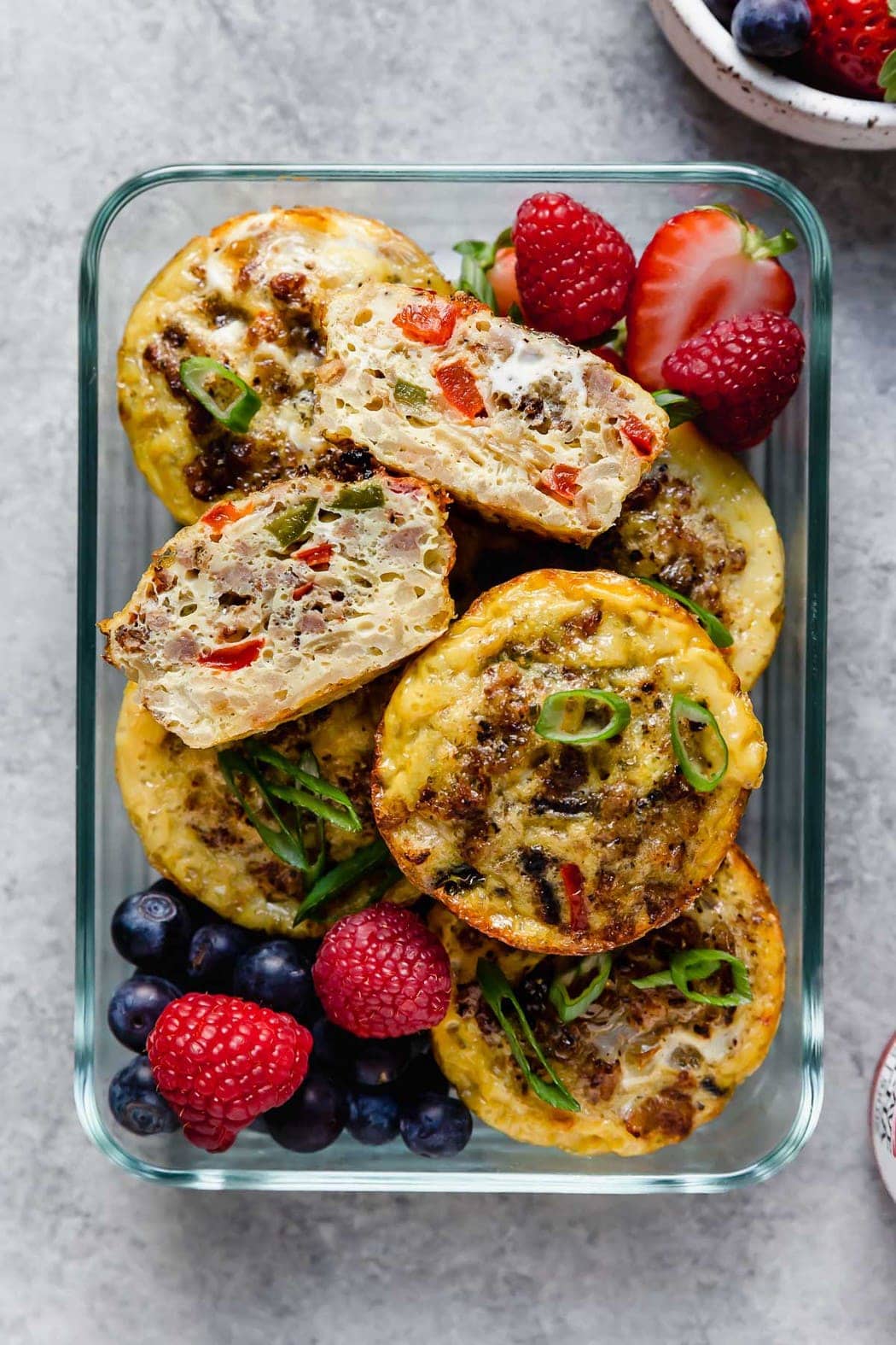 Overhead view of breakfast egg bites and fresh fruit in a glass meal prep container. 