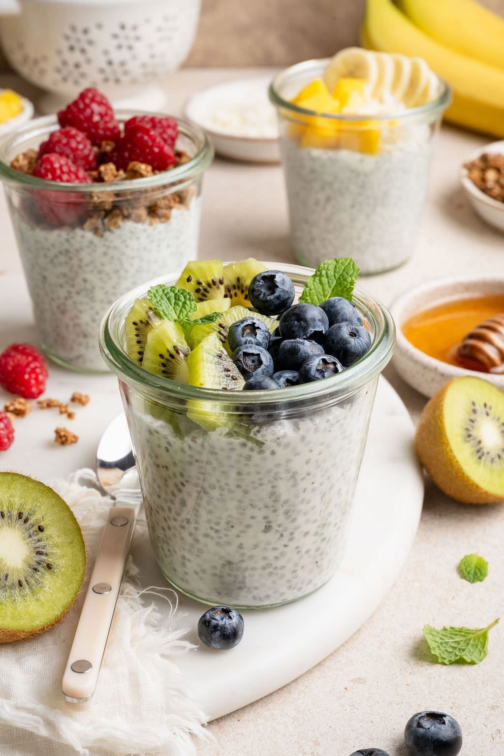 A variety of glass jars filled with chia pudding and topped with different fruits and granola. 
