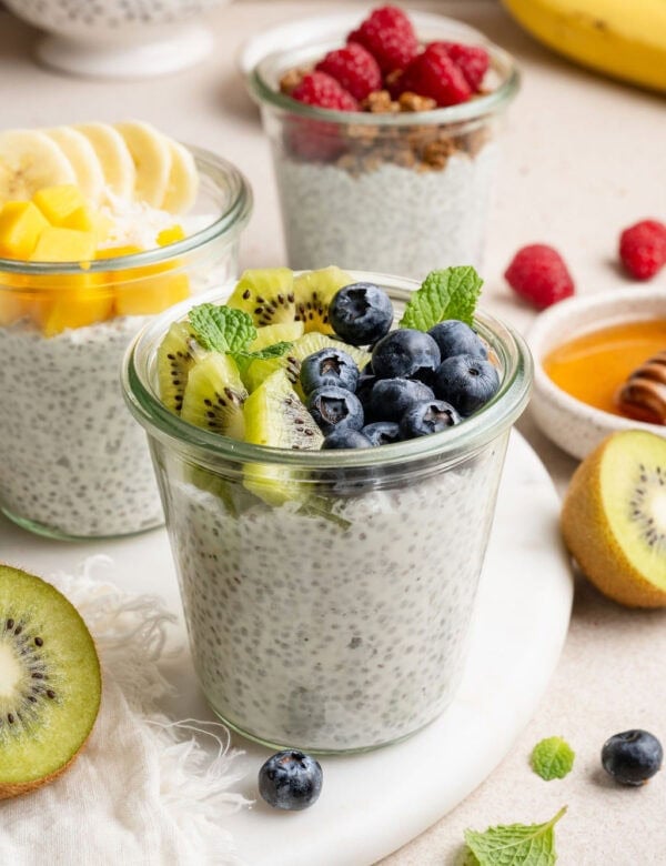 Three short jars filled with chia pudding topped with fresh fruit and mint sprigs