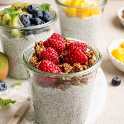 Close up view of a variety of glass jars filled with chia pudding and topped with colorful fresh fruit and crunchy granola.