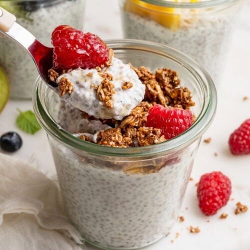 Close up view of a glass jar filled with chia pudding and topped with fresh raspberries and granola.