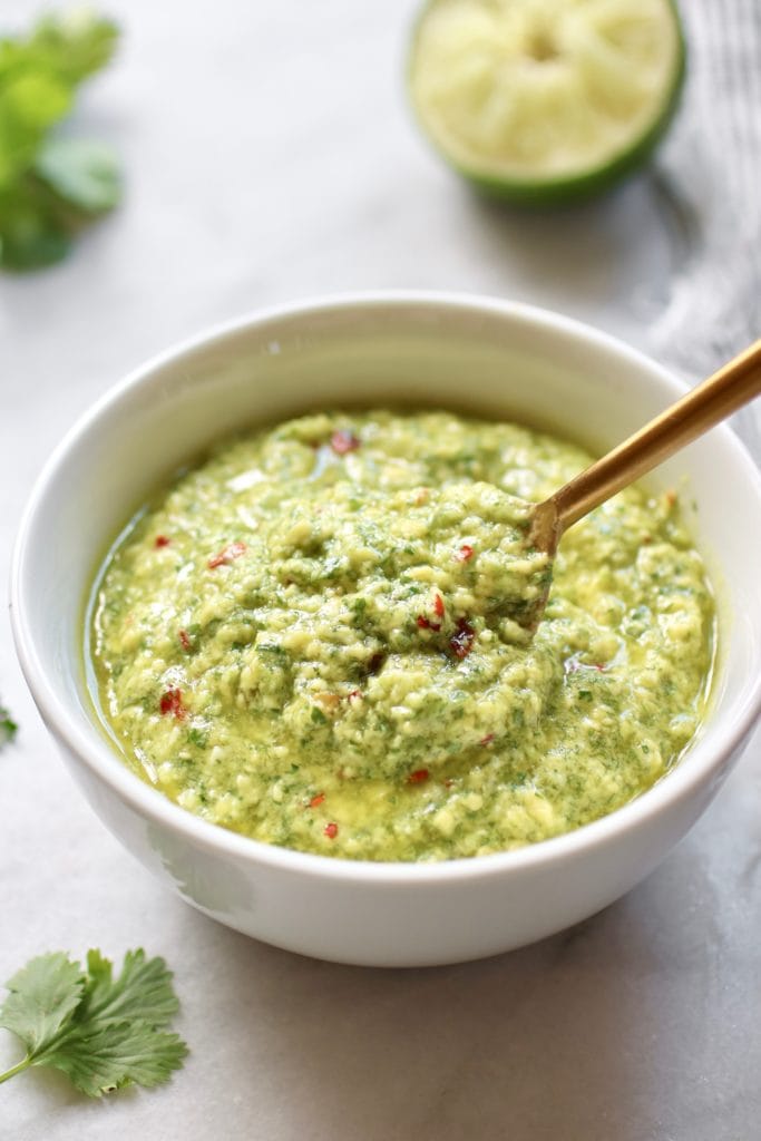 Photo of Avocado Green Sauce in a white bowl with gold spoon in it.