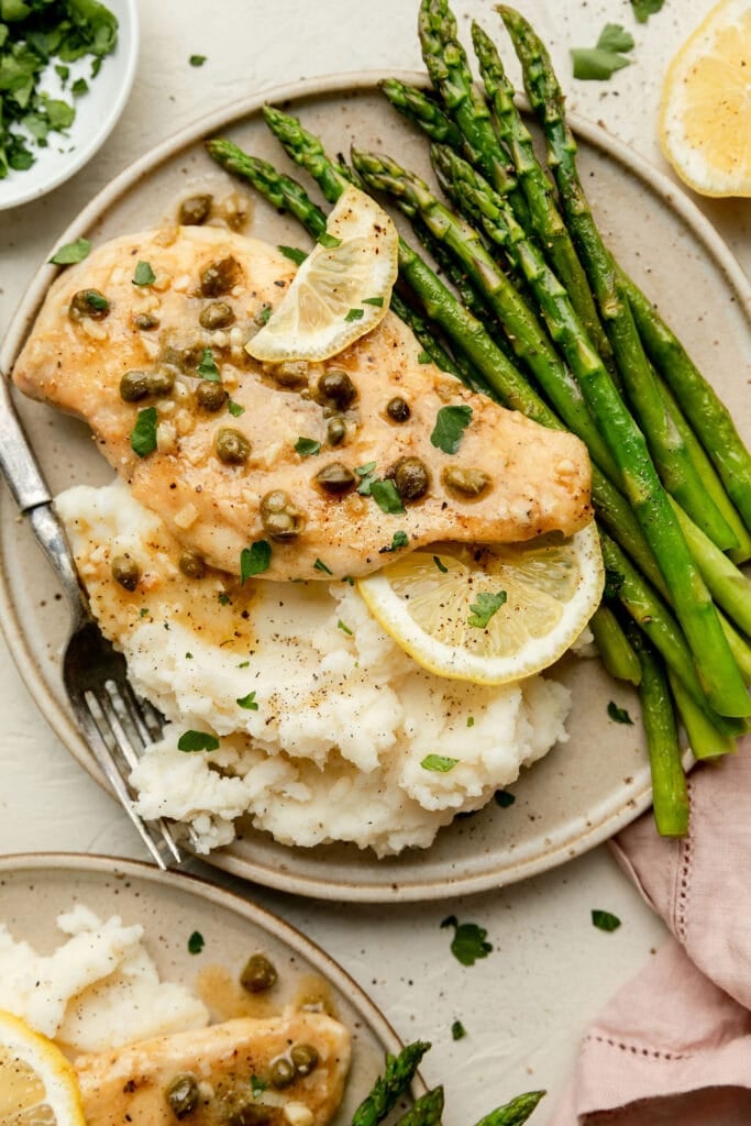 Overhead view of lemon chicken piccata on a plate with mashed potatoes and steamed asparagus.