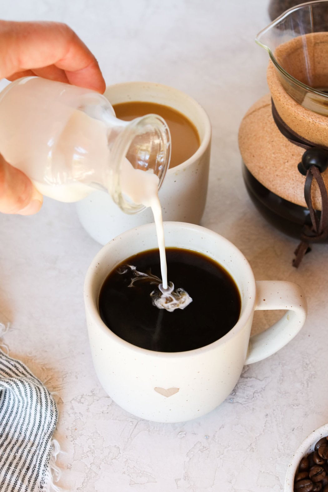 Close up view of a hand pouring cream into a mug filled with coffee.