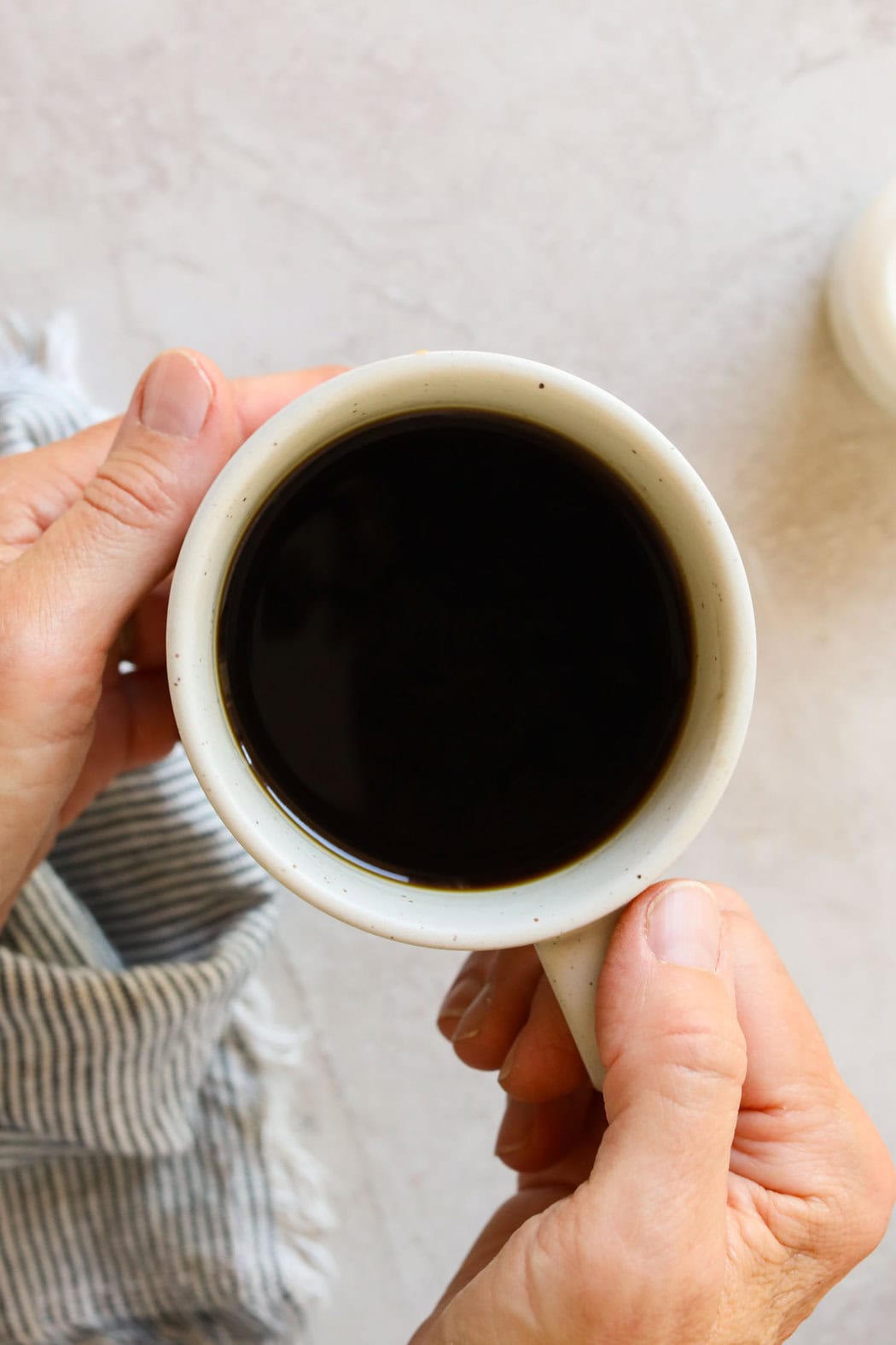 Overhead view of hands holding a coffee mug filled with black coffee.