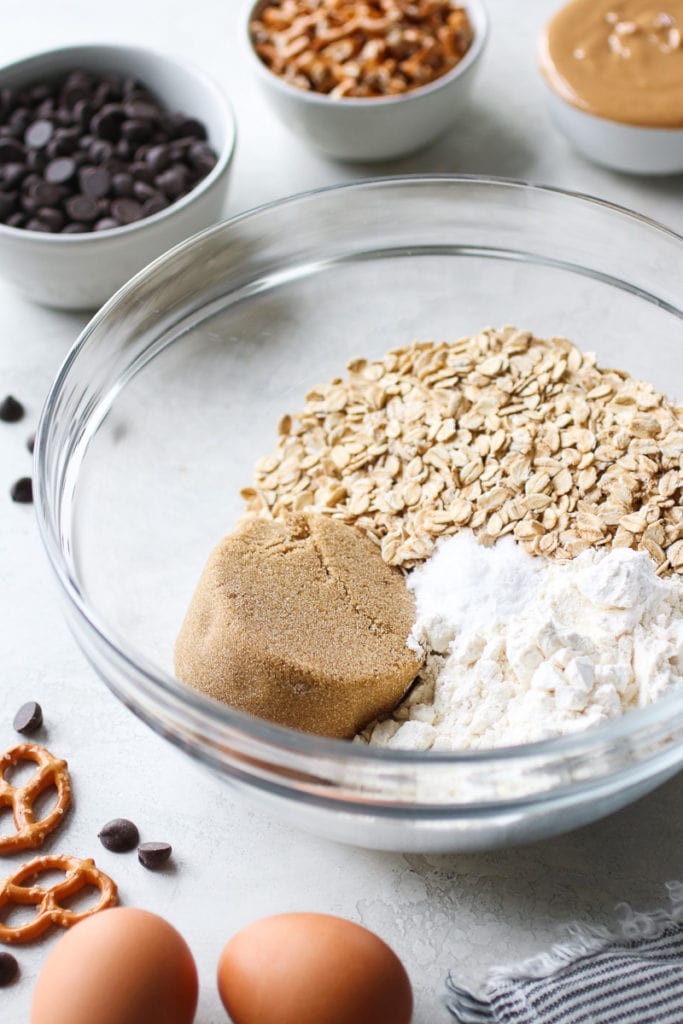 A clear glass bowl with oats, flour, brown sugar, and baking powder.