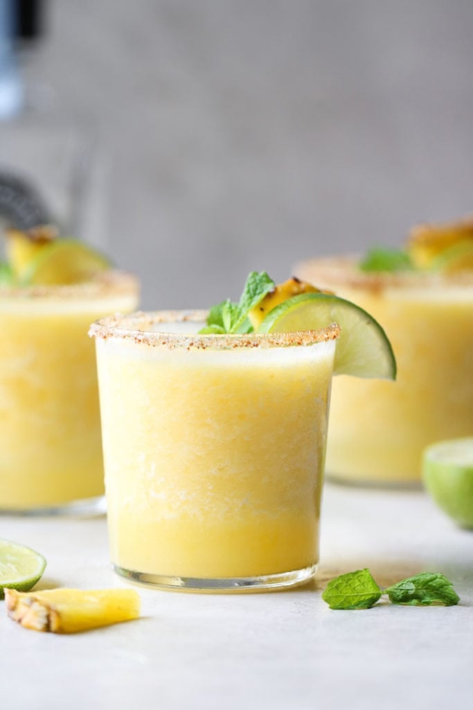 Photo of Frozen Pineapple Margaritas - three servings garnished with a fresh mint leaf, lime slice and pineapple wedge.