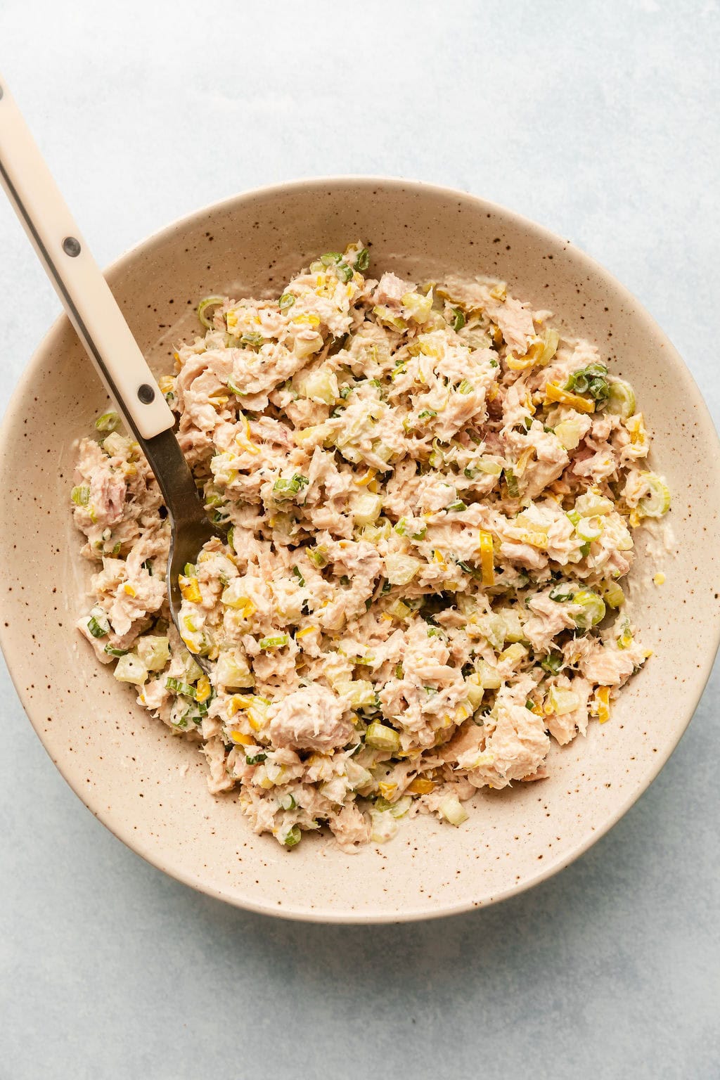 Overhead view of a bowl of tuna salad in a ceramic bowl with a spoon in the side.
