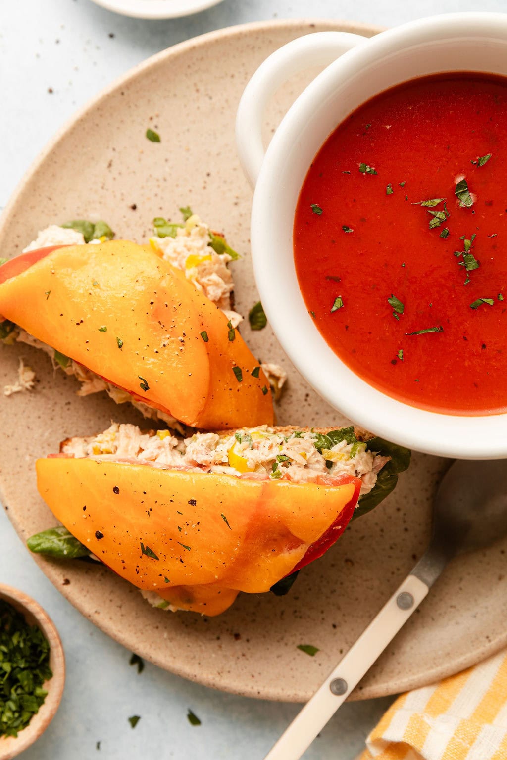 Overhead view of a plate with two open faced tuna melts next to a bowl of tomato soup.