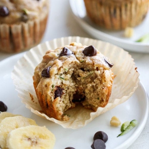 Zucchini banana chocolate chip muffin on paper liner with bite taken from side of muffin.