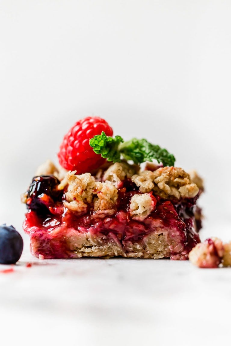 Close up view of a berry oat crumble bar topped with fresh mint and raspberries.
