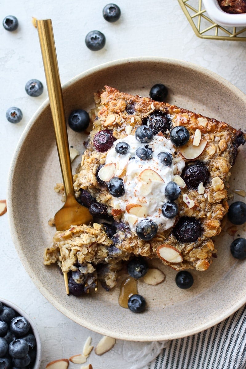 Serving of blueberry baked oatmeal on stone plate topped with whipped cream and fresh blueberries.