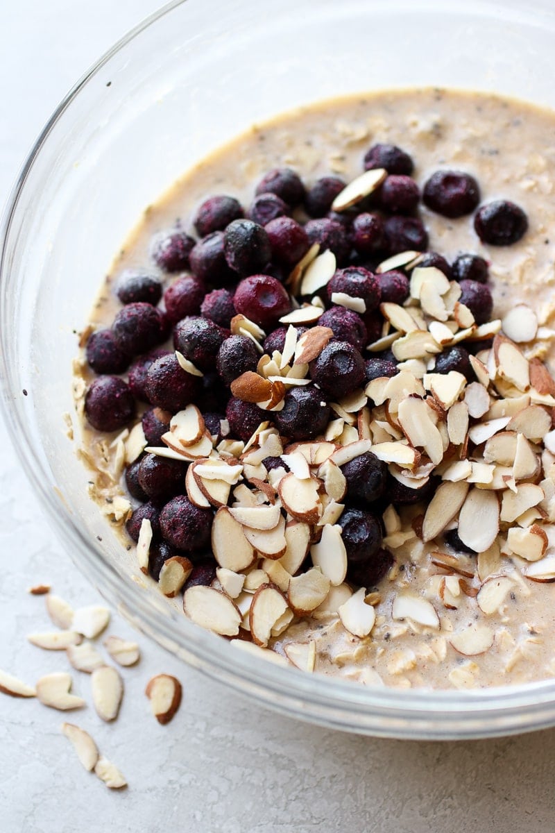 Blueberry Baked Oatmeal ingredients mixed in a bowl with sliced almonds and blueberries onto ready to be mixed in.