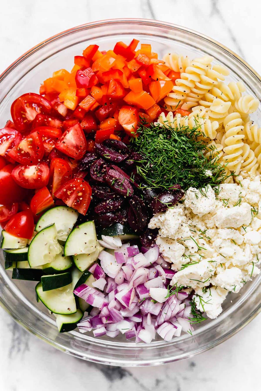 Overhead view of a bowl of Greek Veggie Pasta Salad ingredients.