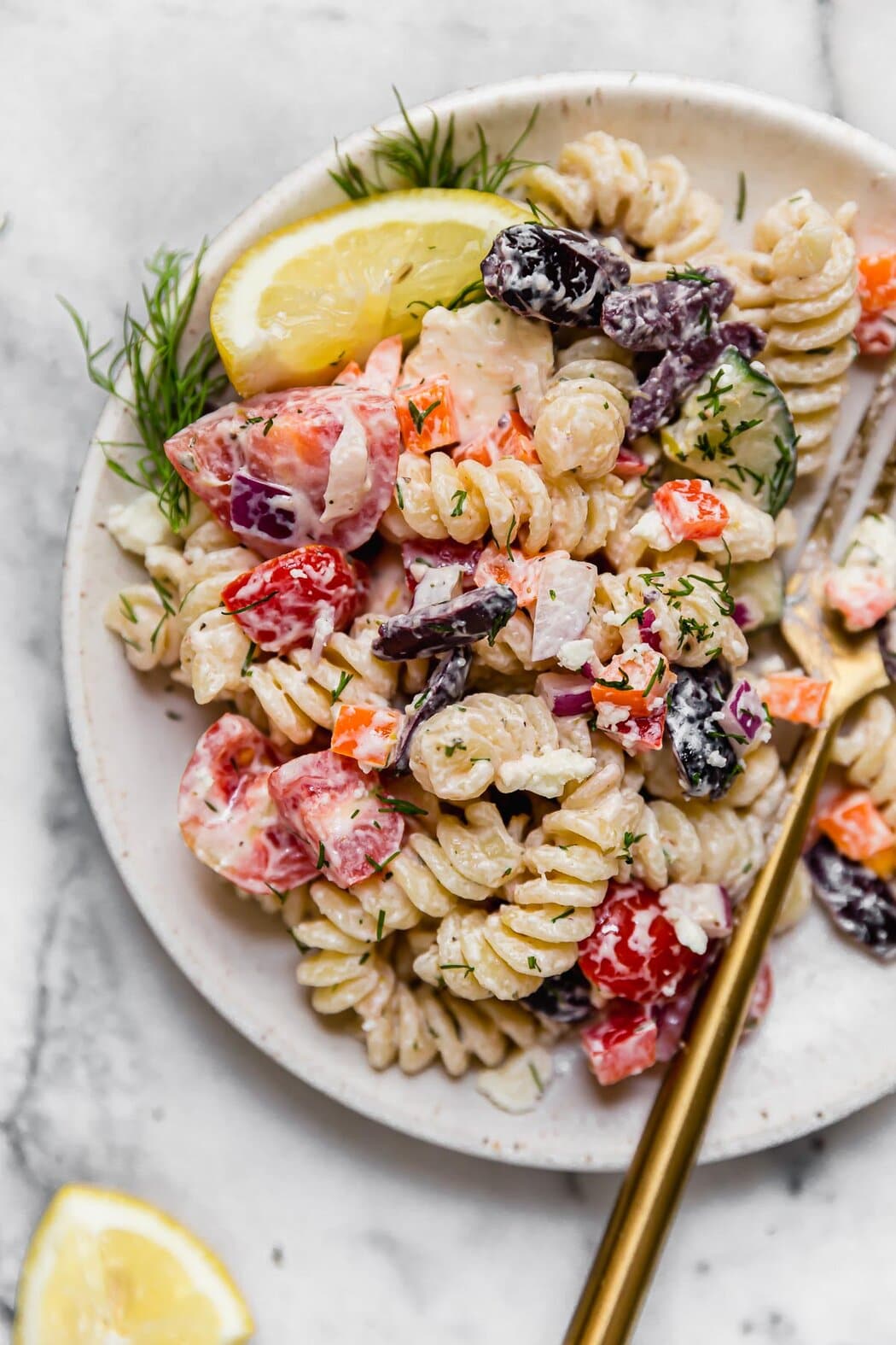 Gluten-free Greek Veggie Pasta with fresh veggies on a white plate with dill and lemon wedges on the edge.