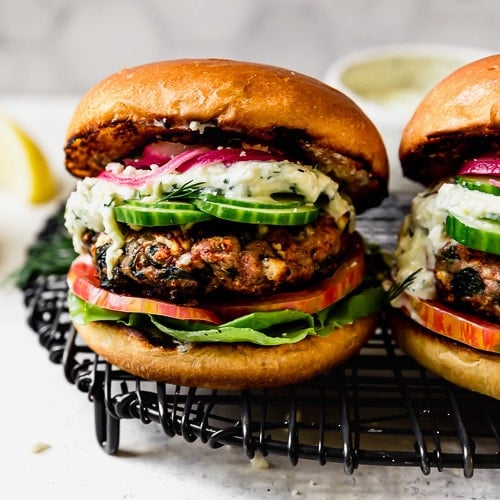 Grilled Turkey Burgers on a wire serving tray. Served in a bun with cucumber, onion, lettuce, tomato and Tzatziki sauce.