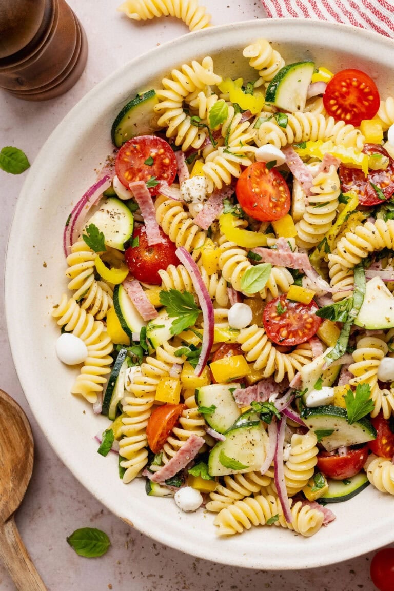 Overhead view of a white bowl filled with a colorful Italian pasta salad topped with fresh zesty dressing.