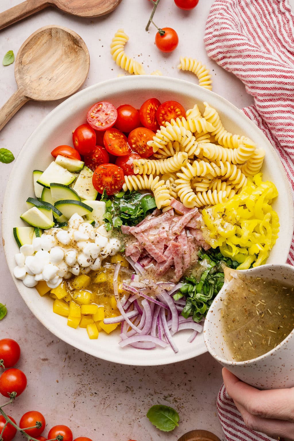 A large bowl of Zesty Italian Pasta Salad arranged in sections with Italian Dressing being poured over the top.