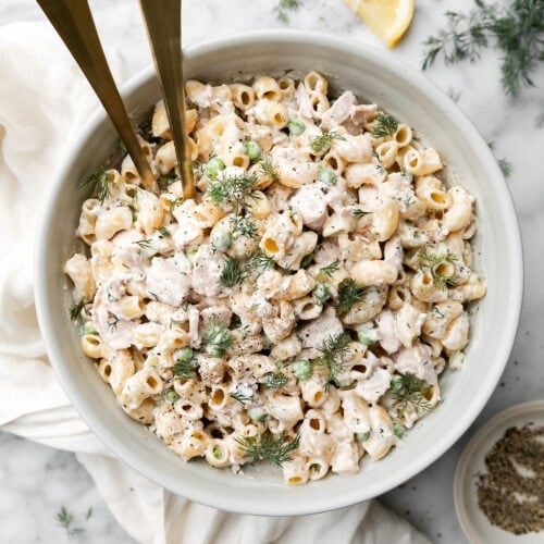 Overhead view white bowl filled with tuna pasta salad with fresh fill sprinkled on top