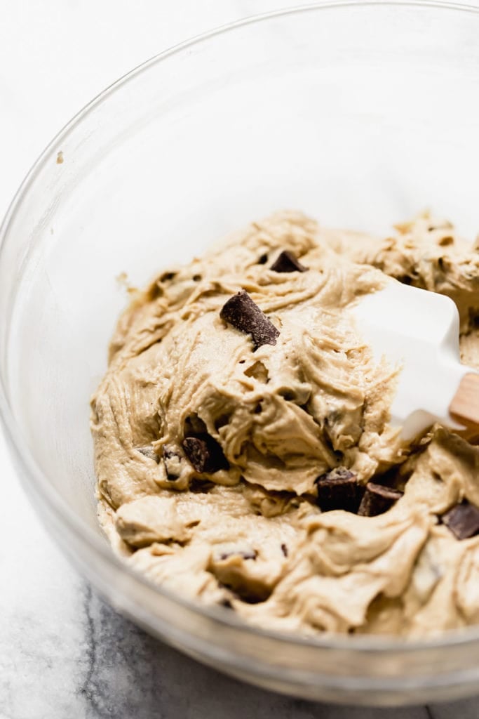 A glass bowl with chocolate chunk cookie dough and a spatula.