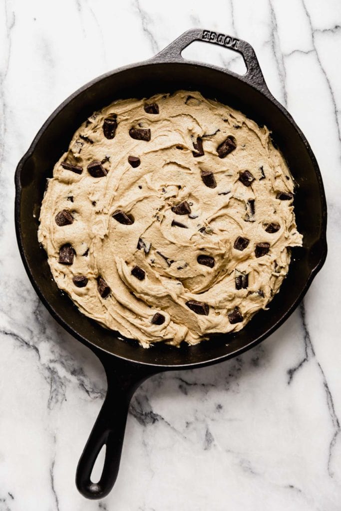 Vegan Chocolate Chunk Cookie dough is spread into a cast iron skillet and ready to bake.
