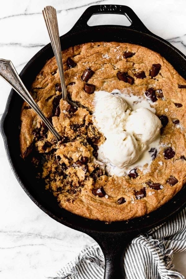 Soft and chewy chocolate chip cookie baked in a cast iron skillet with half melted ice cream on top.
