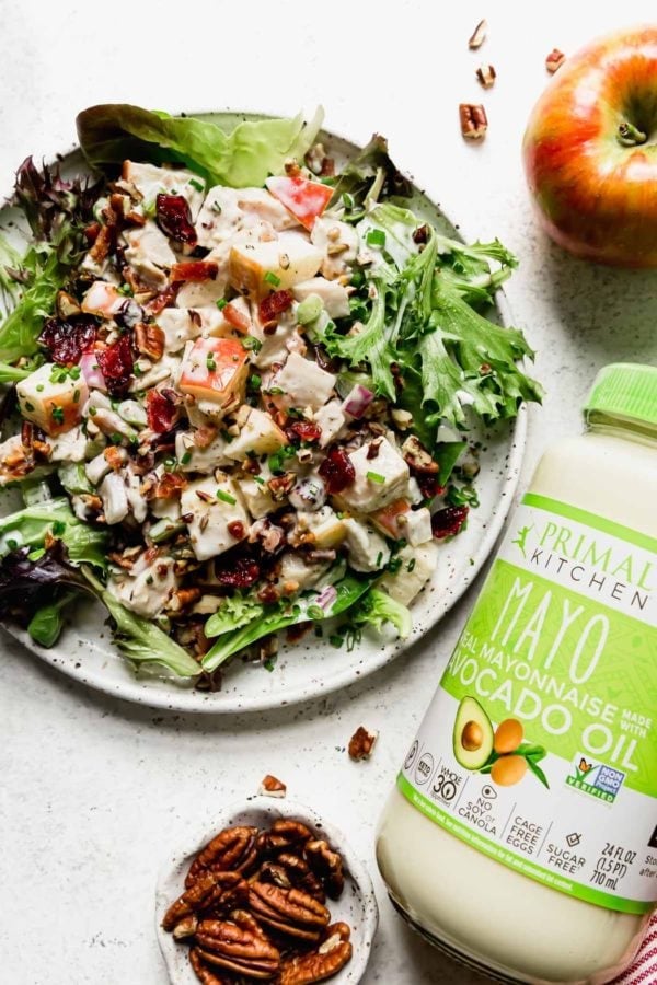 Cranberry Chicken Salad with Apples on a white plate served over a bed of greens with a jar of Primal Kitchen Mayo off to the side.