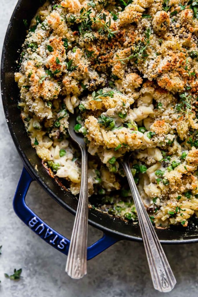 Healthy Tuna Noodle Casserole shown in a blue enameled cast iron skillet with two spoons in it. 