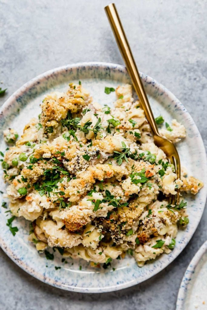 A light grey plate with a serving of Healthy Tuna Noodle Casserole served with a gold fork and garnished with fresh thyme and parsley.