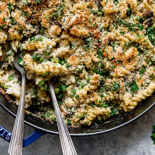 Creamy gluten free tuna noodle casserole in a blue cast iron skillet with two spoons in the casserole ready to serve