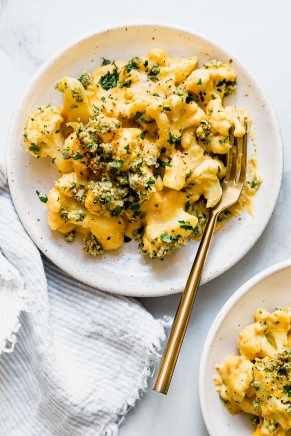 Vegan cauliflower mac and cheese with a grain free bread topping served on a cream plate with a gold fork.