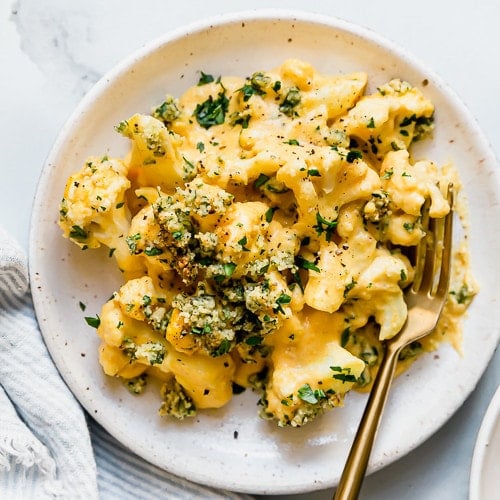 Birds eye view of cauliflower mac and cheese topped with cashew and herb crumble served on a cream plate.