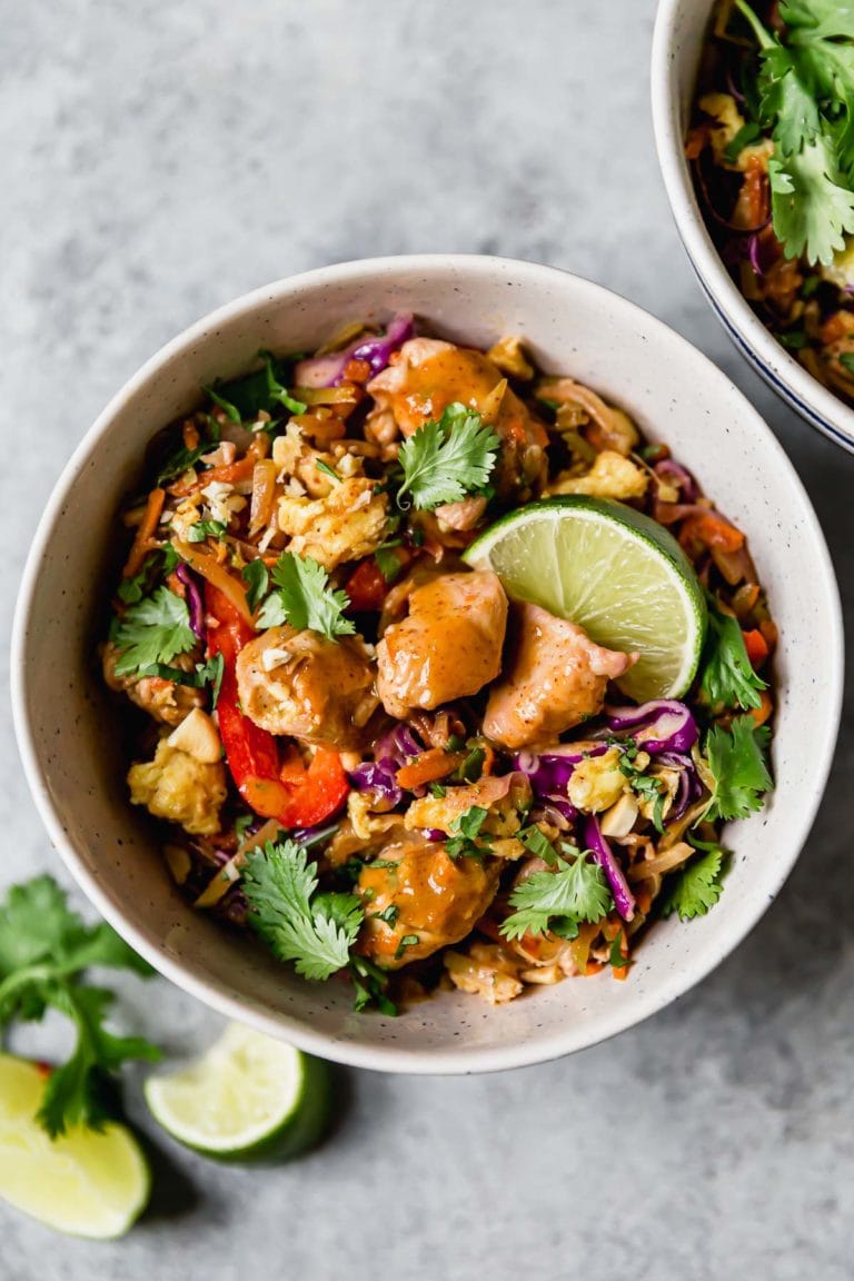 Overhead view white bowl filled with chicken pad Thai topped with cilantro and garnished with a lime wedge.