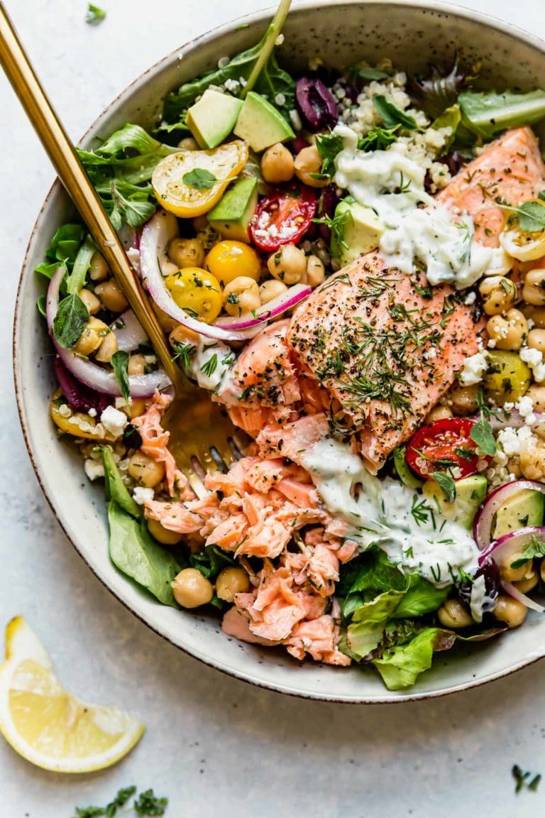 Overhead view of a colorful Mediterranean Bowl with Salmon topped with tzatziki sauce and fresh herbs.