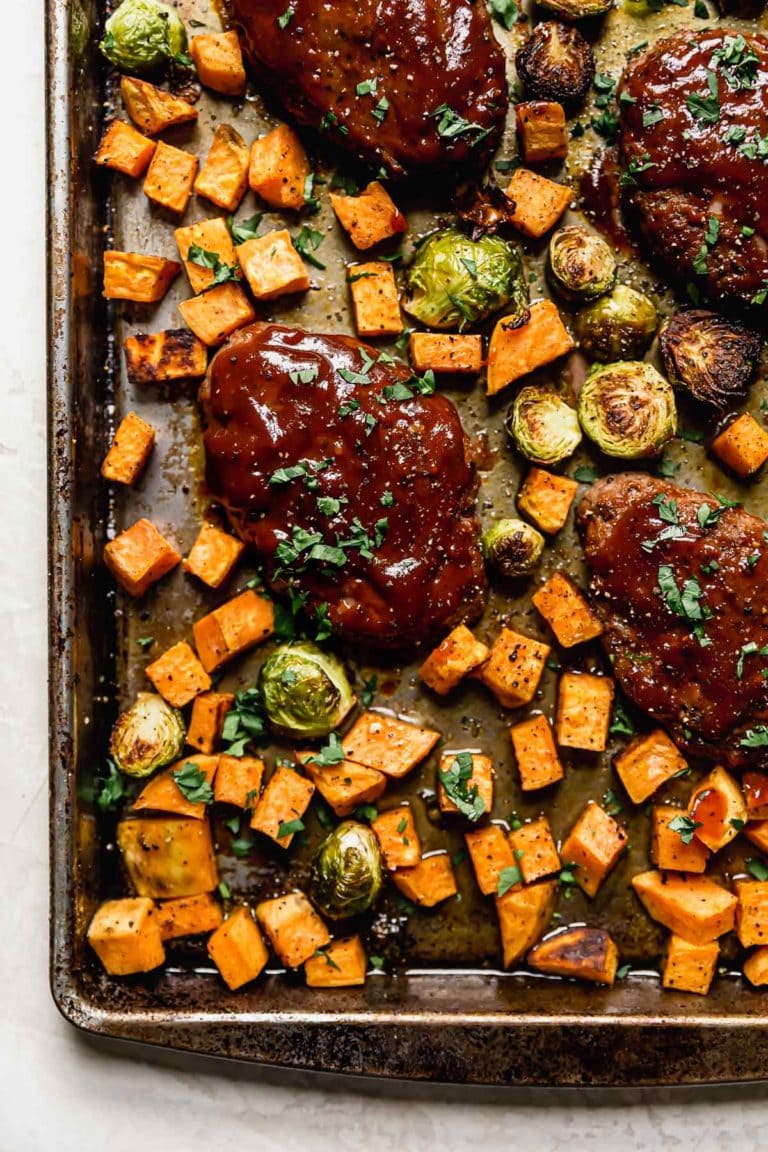 Overhead view of a sheet pan of freshly baked mini meatloaves and sweet potatoes with brussels sprouts surrounding the meat.