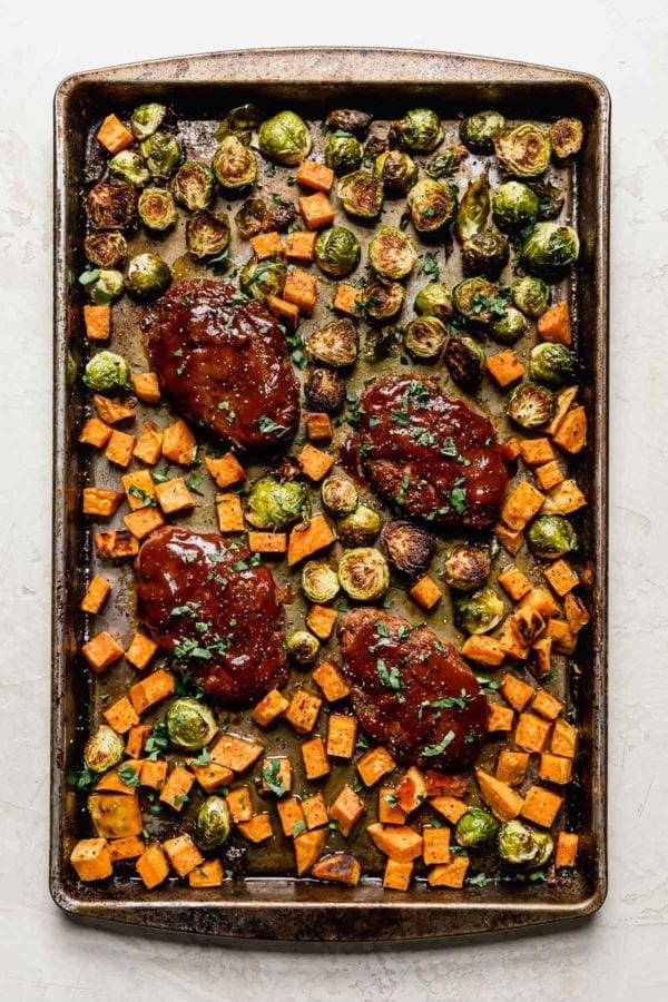 Mini bbq meatloaves and roasted sweet potatoes and brussels sprouts on a baking sheet