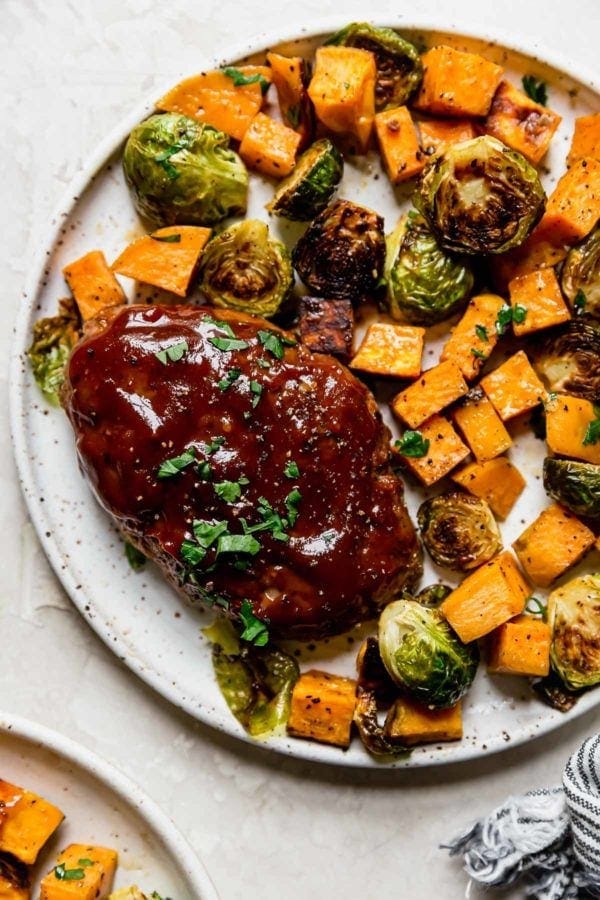 A mini meatloaf with roasted sweet potatoes and brussels sprouts on a speckled plate
