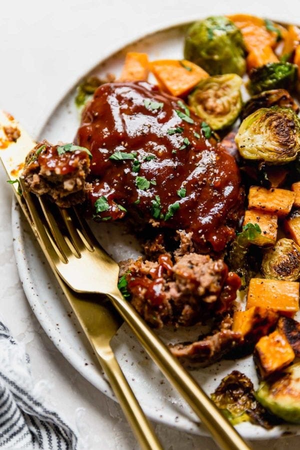 A bbq mini meatloaf on a speckled plate with a piece of meatloaf on a gold fork