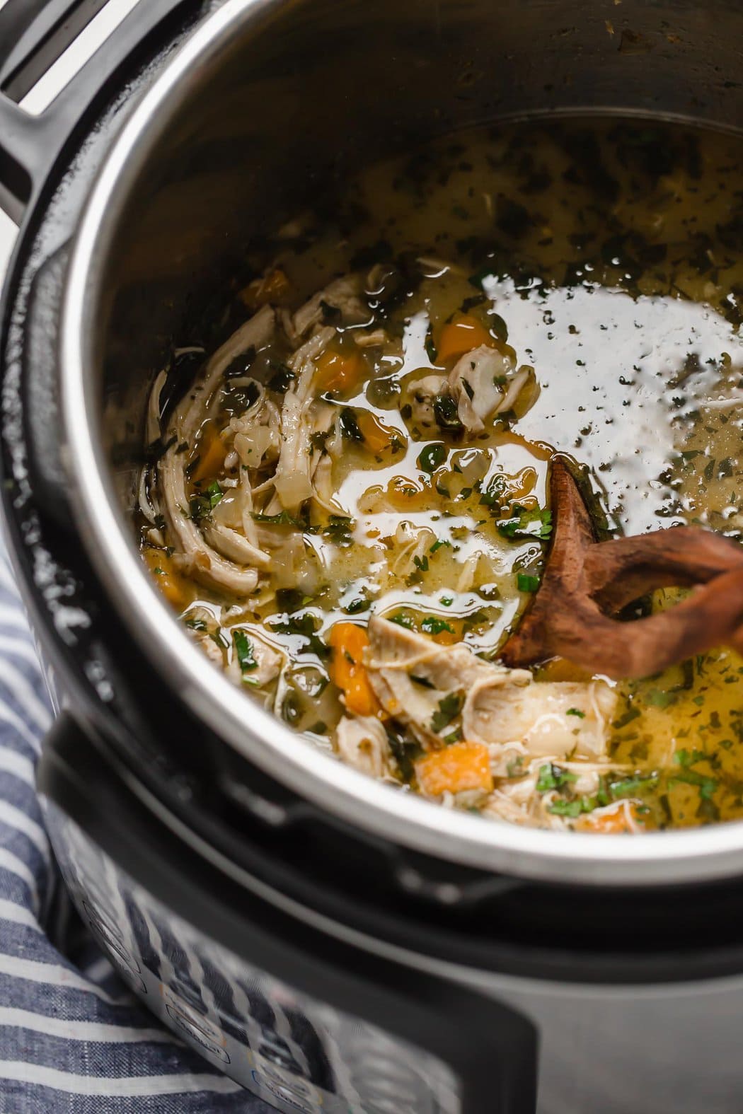 Close up view of a slow cooker filled with Slow Cooker White Chicken Chili (Dairy-Free) and a wooden spoon stirring it. 