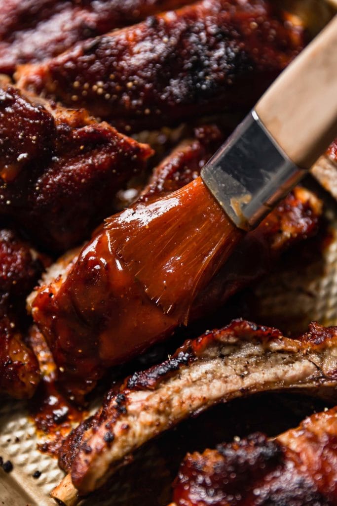 Baby Back Ribs being rubbed with bbq sauce with a brush